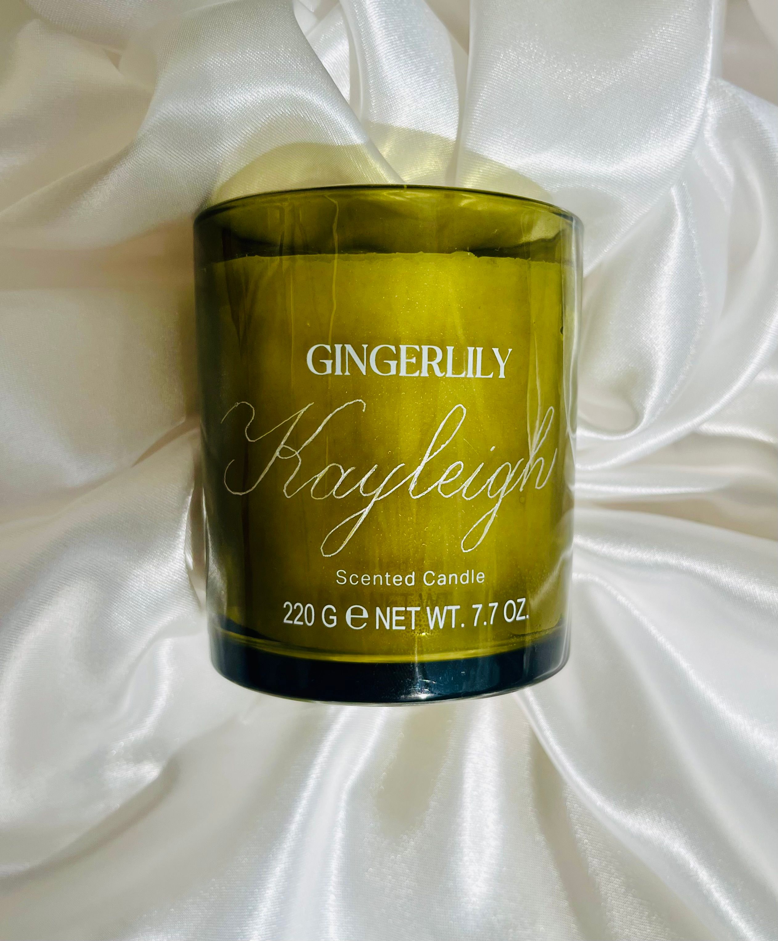 “Kayleigh” hand-engraved in Copperplate script on the olive-green glass of a Gingerlily scented candle, resting on white satin.