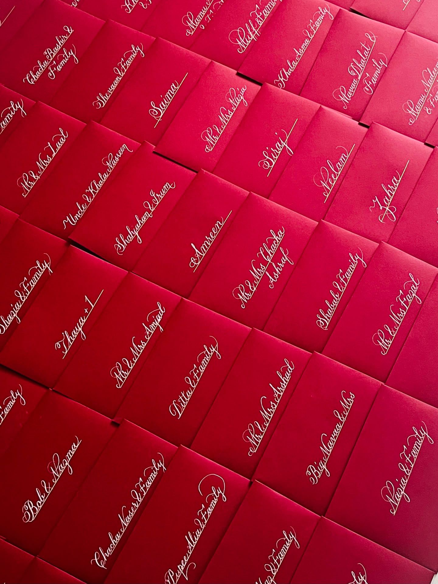 Rows of red envelopes, each hand-lettered in white Copperplate calligraphy with a guest’s name.